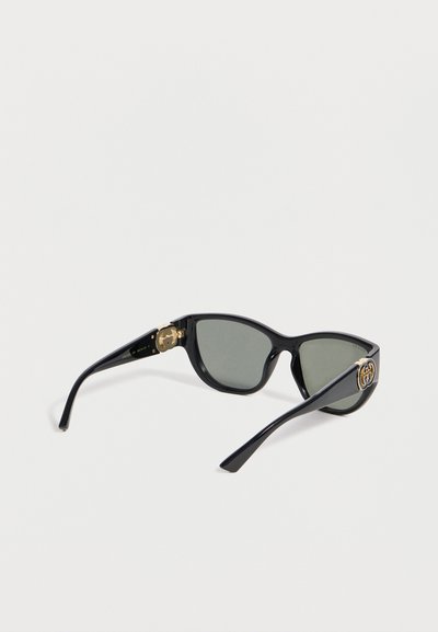 Μαύρα ορθογώνια γυαλιά ηλίου με σκούρους φακούς και χρυσό λογότυπο GG στις βραχίονες, φαίνονται υπό γωνία σε λευκό φόντο.