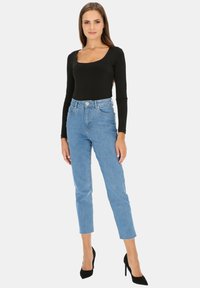 Czarny bodysuit z długim rękawem i kwadratowym dekoltem, zestawiony z jasnoniebieskimi dżinsami o wysokim stanie. Modelka nosi czarne szpilki. Prosty, dopasowany krój.