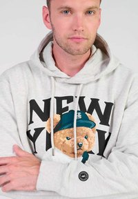 Lichtgrijze hoodie met een berenafbeelding en de tekst "NEW YORK". Voorzien van trekkoorden, een geribde onderkant en een rond logo-op-patch op de mouw.