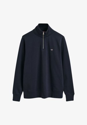 Mörkblå zip-genser med lång ärm och ribbad nederkant, tillverkad av mjukt material. Har en liten logotyp på bröstet.