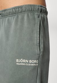 Σκούρες πράσινες φόρμες από μαλακό μίγμα βαμβακιού. Διαθέτουν ελαστική μέση, πλαϊνές τσέπες και κεντητό λογότυπο που γράφει "BJÖRN BORG TRAINING CLUB MONACO."