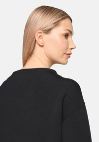 Pull noir à coupe décontractée. Caractéristiques : encolure large, épaules tombantes et texture lisse et douce. Vue de côté montrant une silhouette sans coutures.