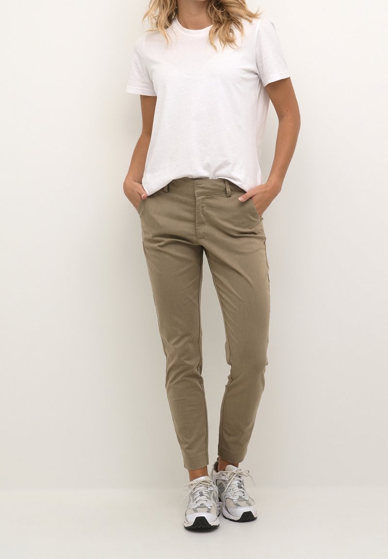 Khaki chinos o slim fit, wykonane z gładkiego materiału. Połączone z gładką białą koszulką i szarymi sneakersami z subtelnymi detalami.