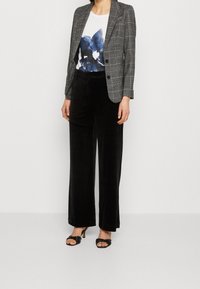 Blazer de cuadros grises sobre una camiseta blanca con un diseño floral azul, combinado con pantalones de terciopelo negros de pierna ancha y sandalias de tacón negras.