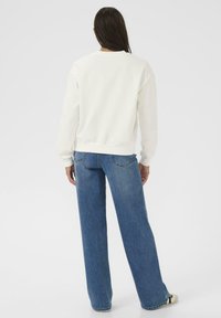 Sweatshirt blanc avec des poignets et un ourlet côtelés, associé à un jean bleu à coupe décontractée. Texture lisse, design minimaliste et sans motifs visibles.