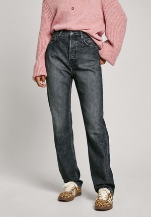Jeans de mezclilla negros de cinturilla alta con un corte recto, combinados con un suéter de punto rosa oversized y zapatillas con estampado de leopardo.