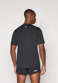 Tricou sport negru, cu mâneci scurte și guler rotund. Prezintă un mic logo alb în zona gâtului din spate. Asortat cu pantaloni scurți negri.
