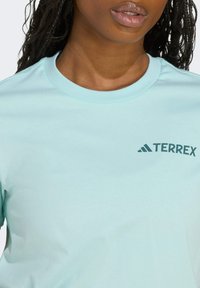 Vaaleansininen puuvillapaita, jossa on pyöreä kaula-aukko ja lyhyet hihat. Vasemmassa rintakorussa tumma sininen "TERREX" -logo.