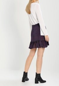 Un haut à manches longues blanc associé à une jupe volantée violette foncée ornée d'un motif floral. Des bottines noires à la cheville complètent l'ensemble.