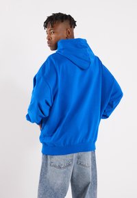 Blå, oversized hettegenser med kengurulomme og snøring i hetta, satt sammen med lyseblå, slitte jeans. Glatt stoff med en avslappet passform.