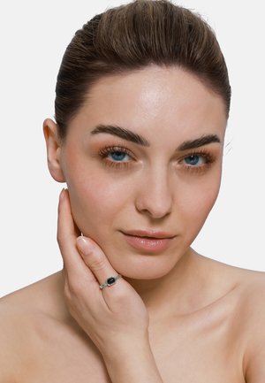 Anello da donna con una pietra nera rettangolare, incastonata in una fascia di argento texturizzato, indossato su una mano che tocca il viso. Pelle liscia, espressione chiara.