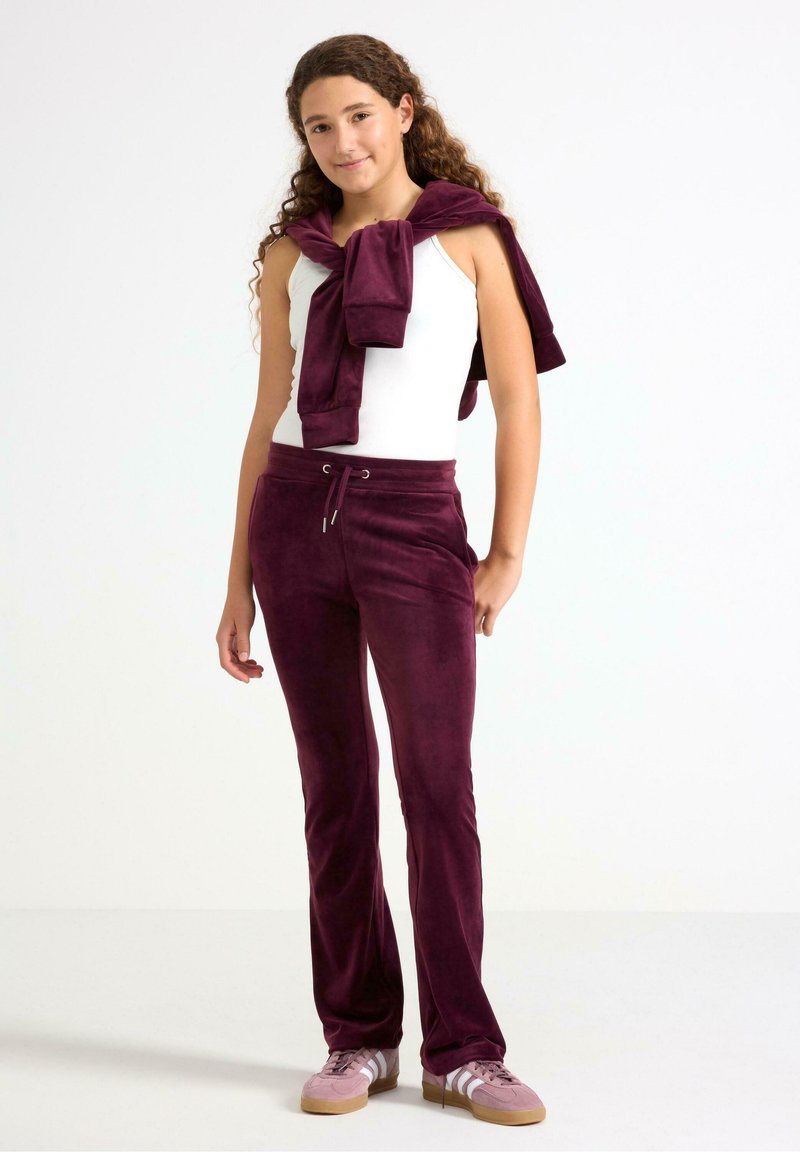 Velvet tracksuit in deep purple with matching pants featuring a drawstring waist. A white tank top and purple sweater tied around the shoulders.