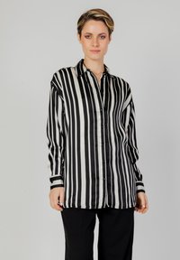 Camicia di seta a righe bianche e nere con chiusura a bottoni, maniche lunghe e dettagli neri ai polsini. Tessuto liscio, vestibilità morbida.