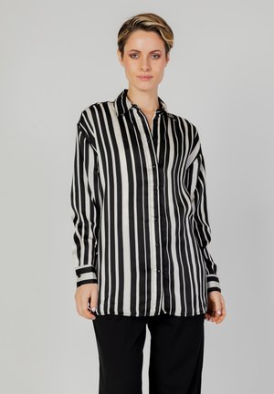 Camicia di seta a righe bianche e nere con chiusura a bottoni, maniche lunghe e dettagli neri ai polsini. Tessuto liscio, vestibilità morbida.