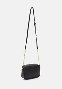 Bolso cruzado rectangular de cuero negro con cadena dorada y correa desmontable, que cuenta con cierre de cremallera y superficie texturizada.
