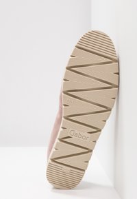 Semelle d'une chaussure beige avec des rainures profondes en zigzag, taille 4½ indiquée, de la marque "Gabor", posée contre un mur blanc et un coin de sol.