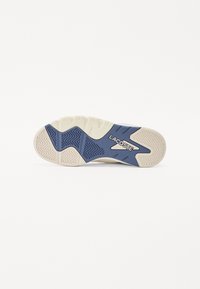 Sohle eines Lacoste-Schuhs mit einer strukturierten weißen Gummibasis und blauen Akzenten, versehen mit dem Schriftzug "LACOSTE" und geometrischen Mustern.
