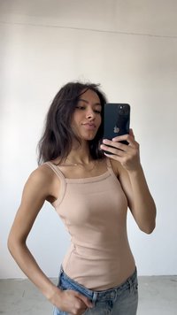 Beige bordázott ujjatlan top négyzet alakú nyakrésszel, világoskék farmernadrággal párosítva. A modell az egyik kezét a csípőjén tartva pózol, tükrözve a laza stílust.