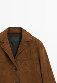 Bruine suède jas met een puntige kraag, knoopsluiting en zichtbare naaddetails, met een zwarte binnenlabel.
