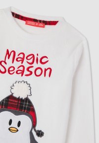 Biała polarowa koszula z długimi rękawami z wizerunkiem pingwina w czerwono-czarną kratkę na czapce. Napis "Magiczny Sezon" jest wyszyty na czerwono nad pingwinem.