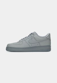 Nike Air Force 1 tenisice u svijetlosivoj boji, izrađene od glatke kože, s ravnim potplatom, okruglim vrhom i perforiranim detaljima na gornjem dijelu.
