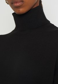 Svart polotröja med en åtsittande design, mjuk textur och ribbad krage. Närbild som betonar hals- och bröstområdet.
