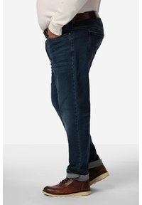 Jeans in denim scuro con taglio dritto, sezioni sbiadite, tasche laterali e orli arrotolati, abbinati a scarpe in pelle marrone.
