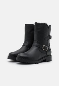 Botas negras de cuero hasta el tobillo con un acabado texturizado, que presentan una correa lateral con hebilla, tacón bajo en bloque y forro de piel sintética en la parte superior.