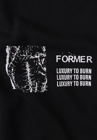Μαύρο μπλουζάκι με λευκό γραφικό τετράγωνο που έχει υφή σχεδίου και το κείμενο "FORMER" και "LUXURY TO BURN" με έντονα, κεφαλαία γράμματα.