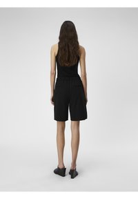 Haut noir sans manches à coupe décontractée, associé à un short noir longueur genou avec une taille élastique et deux poches arrière.