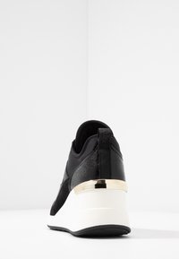 Baskets noires vues de dos avec une semelle plateforme blanche et un accent doré métallique au-dessus de la semelle.