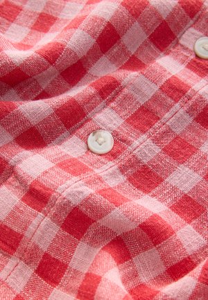 Tissu à carreaux rouges et roses avec une texture douce, présentant des boutons blancs et un design décontracté adapté aux chemises ou blouses.