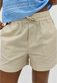Beige linnen shorts met een elastische tailleband, voorzien van een trekkoord, zijzakken en een zachte textuur.
