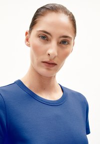 Close-up van een geribbelde, helderblauwe T-shirt met een ronde hals, voorzien van korte mouwen en een gladde textuur. De stof lijkt lichtgewicht te zijn.