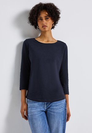 Haut à manches longues navy avec un col rond, fabriqué dans un tissu lisse, associé à un jean bleu clair. Design ajusté et décontracté.