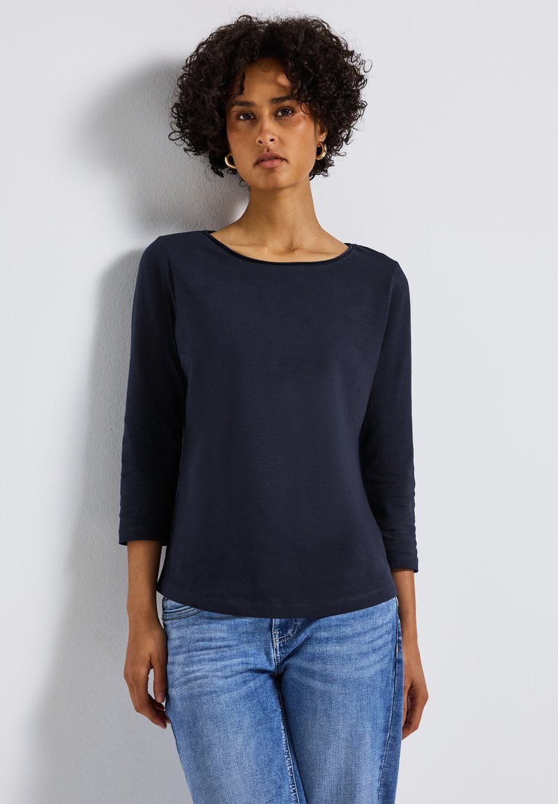 Haut à manches longues navy avec un col rond, fabriqué dans un tissu lisse, associé à un jean bleu clair. Design ajusté et décontracté.