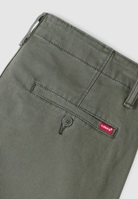 Πράσινο βαμβακερό παντελόνι με υφή, που διαθέτει πίσω τσέπη, κλείσιμο με κουμπί και κόκκινη ετικέτα λογότυπου Levi's.