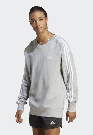 Sudadera gris claro con acentos de tres rayas blancas en las mangas y pequeño logo en el pecho. Textura suave, corte relajado, puños y dobladillo acanalados.
