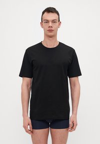 T-shirt nera in cotone con maniche corte, scollatura rotonda e una texture liscia, indossata sopra biancheria intima blu scuro.