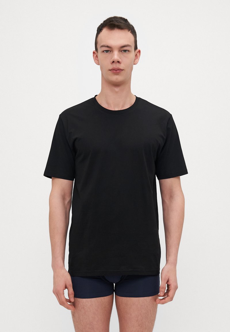 Zwarte katoenen t-shirt met korte mouwen, ronde halslijn en een gladde textuur, gedragen over marineblauwe ondergoed.