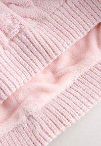 Roza pletena tkanina z rebrasto teksturo in mehko podlogo pod njo. Material je videti udoben in puhast z nežnim sijajem.