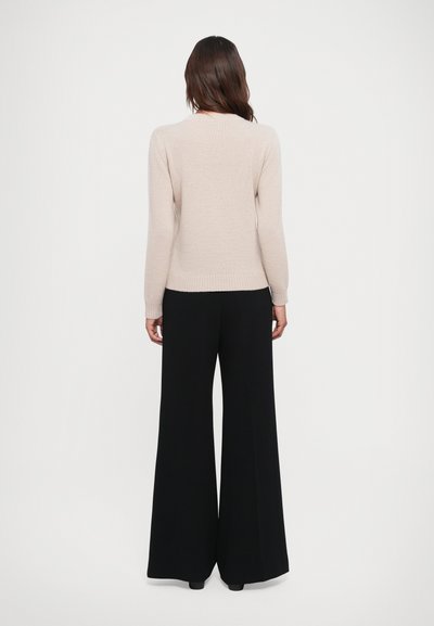Beige knitted sweater with long sleeves, ribbed cuffs, and waistband, paired with high-waisted black wide-leg trousers.