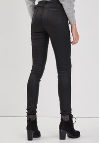 Jean slim noir avec une texture lisse, taille mi-haute et design à cinq poches. Porté avec des bottines à talons noirs.