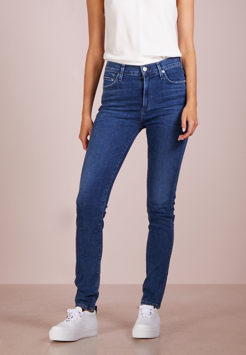 Hubené modré džíny s předními kapsami a klasickým designem pěti kapes. Nosí se s bílými teniskami, které mají hladký povrch.