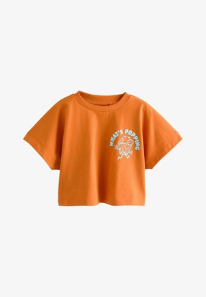 Oranssi lyhyt t-paita pyöreällä kaula-aukolla ja grafiikka, jossa juokseva popcorn-laatikko ja vasemmalla etupuolella sinisellä teksti "WHAT'S POPPING".