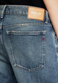 Blå denimbukser med en strukturert finish, som har en lær Replay-label på baksiden av linningen og en liten rød logo over lommen.