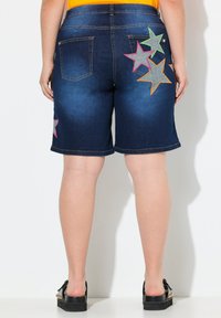 Pantalones cortos de mezclilla con un lavado azul oscuro, que presentan bordados de estrellas multicolores en los bolsillos traseros. Con una longitud hasta el muslo y un ajuste relajado.