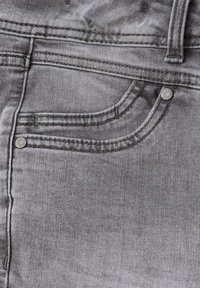 Tejido de denim gris que presenta un bolsillo delantero con doble costura y dos remaches metálicos, mostrando una superficie ligeramente texturizada.