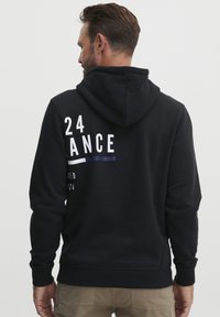 Felpa con cappuccio nera caratterizzata da grafiche testuali bianche e blu navy sulla schiena. Realizzata in tessuto morbido e strutturato. Vestibilità casual con polsini a costine.