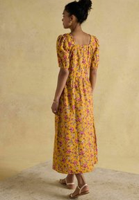 Kollane lilleline midi kleit puffed varrukatega, kitsas vöökoht ja ruudukujuline selg. Omab värvikirevat lillemustrit punaste ja siniste aktsentidega.